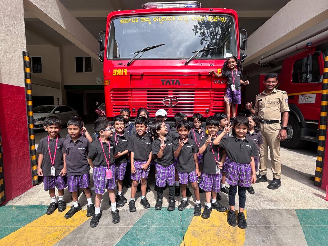 Group of Montessori students posing with firefighters in front of a fire truck during an educational trip at one of the best Montessori schools in Bangalore.